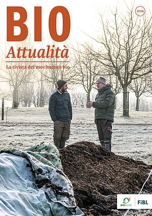 Copertina di Bioattualità 3|24: Due uomini in conversazione sono in piedi in un campo, con alberi sullo sfondo e un cumulo di compost in primo piano.