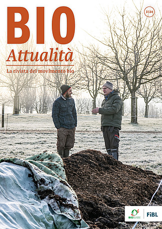 Copertina di Bioattualità 3|24: Due uomini in conversazione sono in piedi in un campo, con alberi sullo sfondo e un cumulo di compost in primo piano.